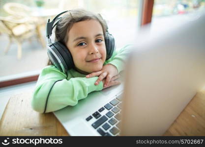 Portrait of cute girl listening to music on headphones with laptop at table