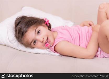Portrait of Cute girl lying on a bed with pacifier in her mouth. Selective focus and small depth of field.. Portrait of Cute girl lying on a bed with pacifier