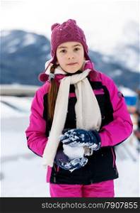 Portrait of cute girl playing in snowballs on top of high mountain