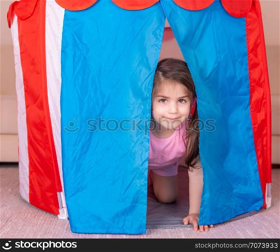 Portrait of Cute girl plays hiding in a colorful toy tent. Selective focus and small depth of field.. Portrait of Cute girl plays hiding in a colorful toy tent