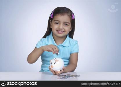 Portrait of cute girl putting coins in piggy bank against blue background