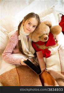Portrait of cute girl reading book to teddy bear at bed