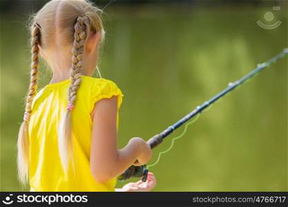 Portrait of cute girl sitting at bank and fishing