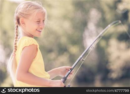 Portrait of cute girl sitting at bank and fishing