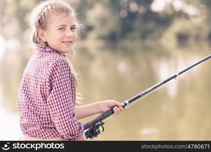 Portrait of cute girl sitting at bank and fishing