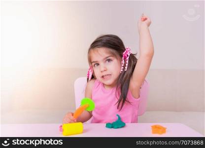 Portrait of Cute girl throwing playdough while sitting on table. Selective focus and small depth of field.. Portrait of Cute girl playing with toys for playdough
