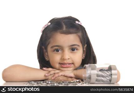 Portrait of cute girl with Indian coins spilled on table over white background