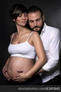 Portrait of cute happy couple expecting baby over black background, future parents hugging with closed eyes of pleasure, love and happiness concept