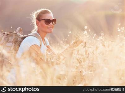 Portrait of cute happy traveler girl in dry ripe wheat field, looking away and enjoying beautiful agricultural view, autumn season