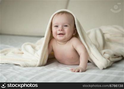 Portrait of cute laughing baby lying under blanket on bed