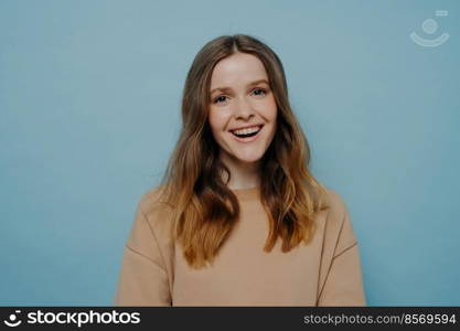 Portrait of cute laughing european teenage girl dressed in casual clothes smiling at camera with positive face expression while standing isolated blue background. Happy people concept. Happy teenage girl looking at camera with positive expression