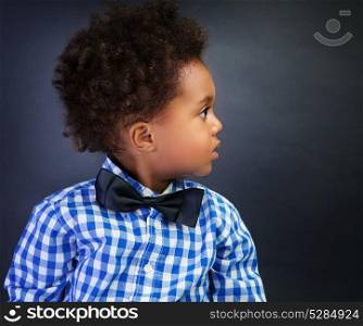 Portrait of cute little African schoolboy with surprise looking in side, over blackboard background, back to school