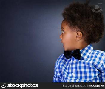 Portrait of cute little African schoolboy with surprise looking in side, over blackboard background, copy space, back to school
