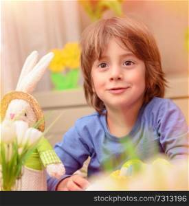 Portrait of cute little baby boy sitting in daycare and play with soft bunny toy and colorful eggs, with pleasure preparing to happy Easter holiday