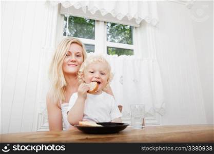 Portrait of cute little boy eating bread with mother at home