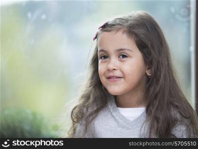Portrait of cute little girl against glass window at home