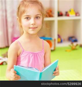 Portrait of cute little girl in daycare with book in hands preparing to go to elementary school, start of education season