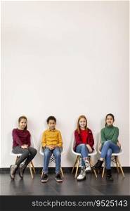 Portrait of cute little kids in jeans  sitting in chairs against the white wall