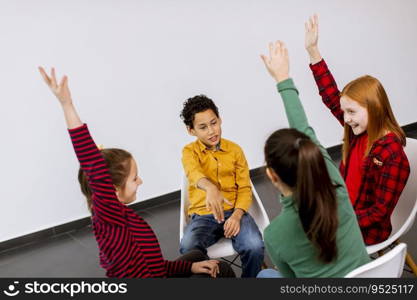 Portrait of cute little kids in jeans talking and sitting in chairs against the white wall