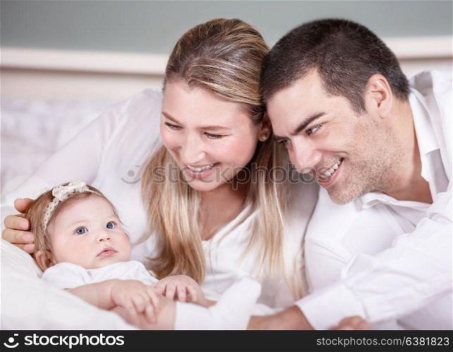 Portrait of cute loving family at home, young parents enjoying time spending with their newborn adorable daughter