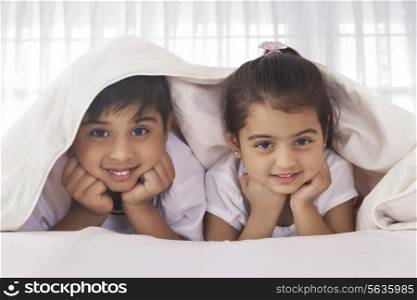 Portrait of cute siblings under blanket in bed