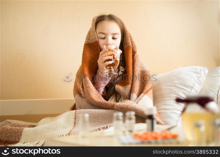 Portrait of cute sick girl covered in blanket drinking hot tea