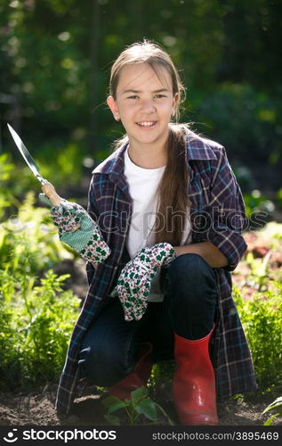 Portrait of cute smiling girl in gloves and gumboots posing at garden