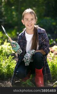 Portrait of cute smiling girl in gloves and gumboots posing at garden