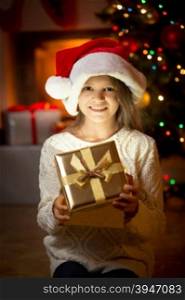Portrait of cute smiling girl posing against fireplace and Christmas tree with gift box