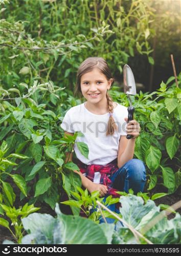 Portrait of cute smiling girl posing with trowel at blooming garden