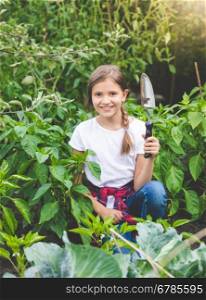 Portrait of cute smiling girl posing with trowel at blooming garden