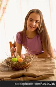 Portrait of cute smiling girl sitting at table with Easter eggs
