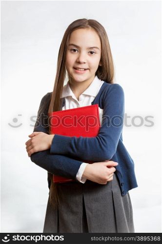 Portrait of cute smiling schoolgirl posing with red book against isolated background