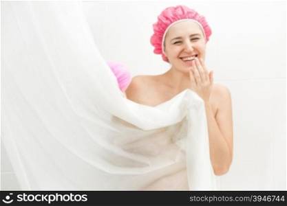 Portrait of cute smiling woman having shower and hiding behind curtain