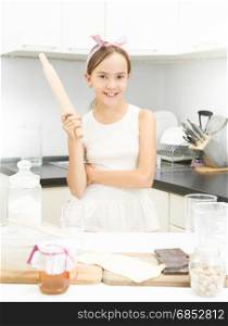 Portrait of cute teen girl posing with wooden rolling pin on kitchen