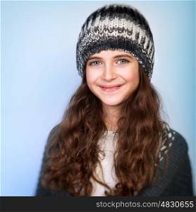 Portrait of cute teen girl wearing stylish knitted hat and sweater isolated on blue background, winter fashion for teenagers