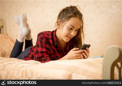 Portrait of cute teenage girl lying on bed and typing message on phone