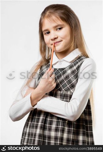 Portrait of cute thoughtful schoolgirl chewing pencil against white background