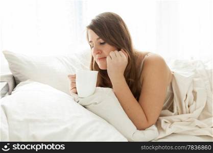 Portrait of cute woman lying in bed with cup of coffee