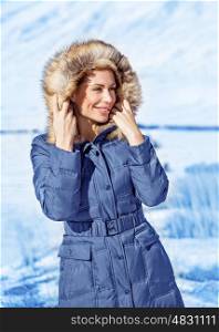 Portrait of cute woman wearing warm coat with hood with fur, having fun in winter park, wintertime fashionable style, vacation concept&#xA;