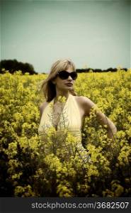 portrait of cute young blond woman outdoor in a yellow field wearing sun glasses with falsed color