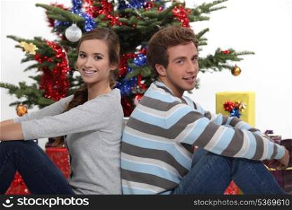 portrait of cute young couple sitting back to back at Christmas time