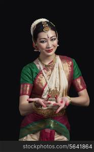Portrait of dancer gesturing while performing Bharatanatyam against black background