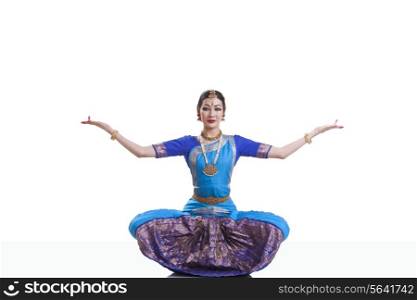 Portrait of dancer with arms outstretched performing Bharatanatyam against white background