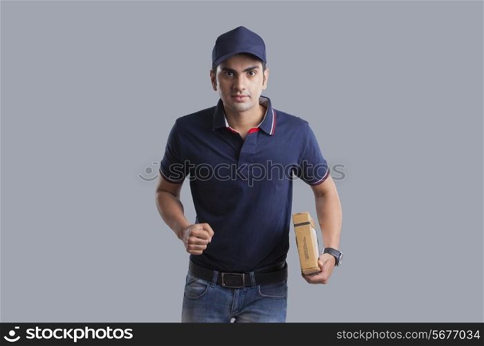 Portrait of delivery man running with package against gray background