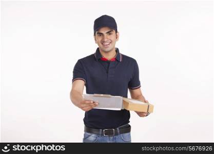 Portrait of delivery man with cardboard box and clipboard against white background