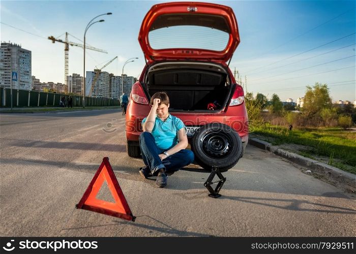 Portrait of depressed man leaning against broken car