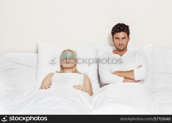 Portrait of displeased man with woman sleeping in bed