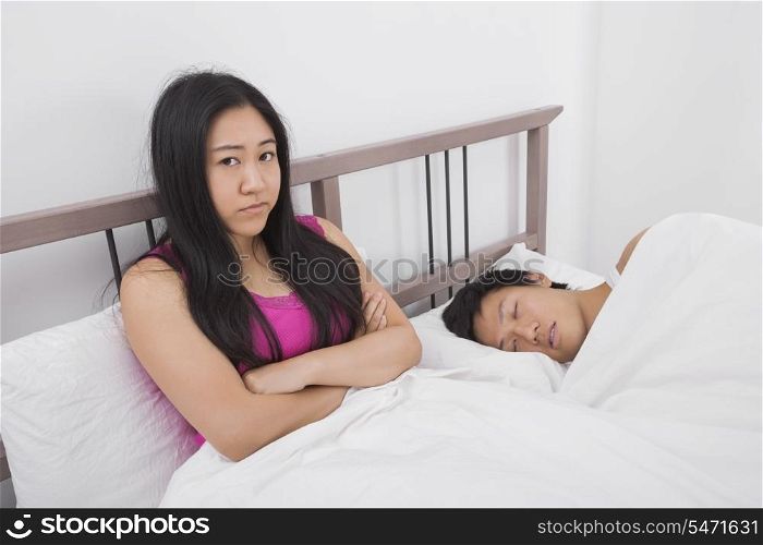 Portrait of displeased woman with man sleeping in bed