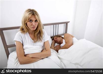 Portrait of displeased woman with man sleeping in bed